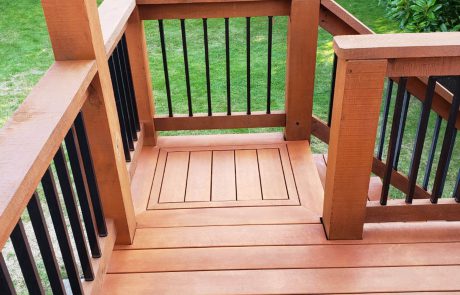 Stained deck with black metal rail supports of a house overlooking a backyard garden