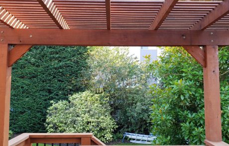 Stained deck with black metal rail supports of a house overlooking a backyard garden