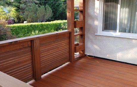 Stained deck with black metal rail supports of a house overlooking a backyard garden