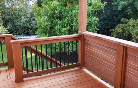 Stained deck with black metal rail supports of a house overlooking a backyard garden