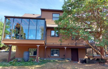 The back view of a brown siding house with solarium and a large tree