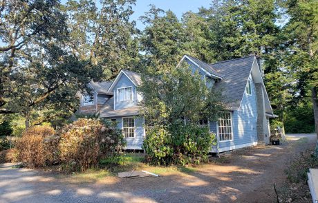 Exterior of a blue house with trees in the front yard in Metchosin Victoria