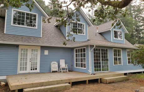 Exterior of a blue house with white frames and a back deck in Metchosin