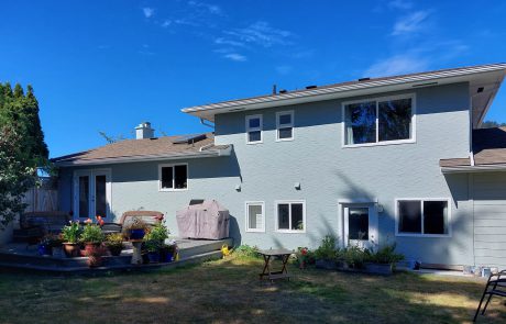 The back yard of a grey house with a deck and lawn