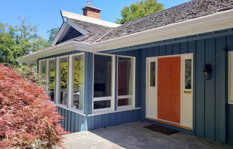 Blue painted house with white window frames and a orange painted front door