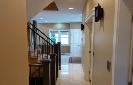 hallway of a home with tan painted walls and white tiled flooring