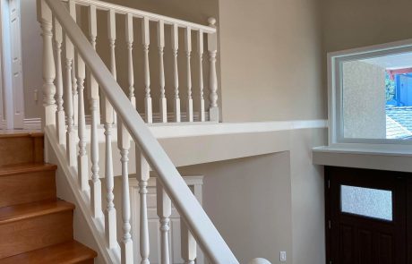 white wooden railing staircase overlooking entrnce of a home with a dark wood door